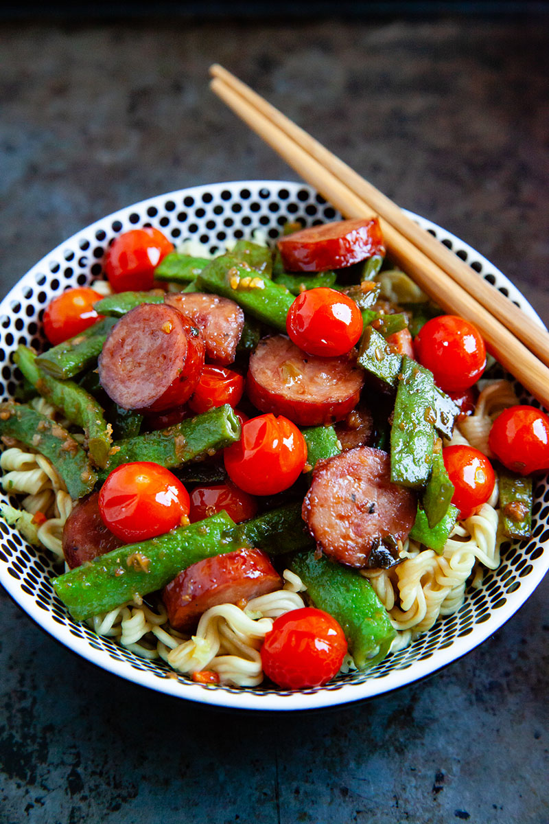 A single serving bowl of noodles with green beans, sausage and cherry tomatoes