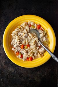 overhead view of chicken noodle soup in a yellow bowl