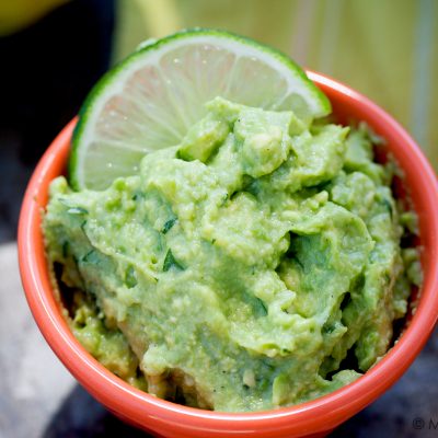 guacamole garnished with a lime wedge in an orange bowl