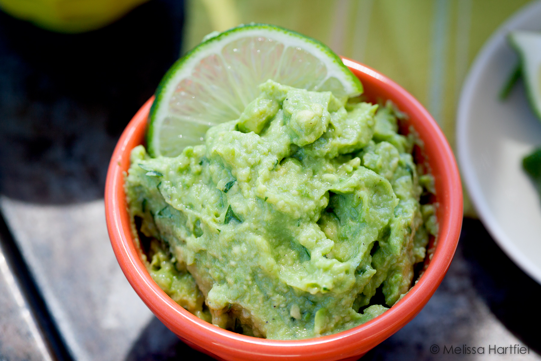 guacamole garnished with a lime wedge in an orange bowl