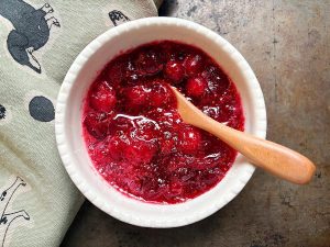 Overhead view of a small white bowl filled with cranberry sauce and a small wooden spoon.