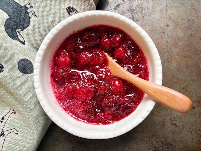 Overhead view of a small white bowl filled with cranberry sauce and a small wooden spoon.