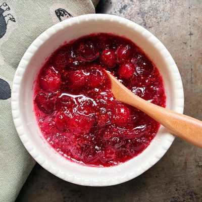 Overhead view of a small white bowl filled with cranberry sauce and a small wooden spoon.