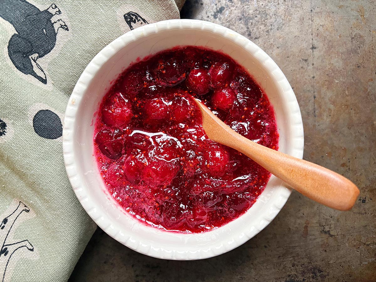Overhead view of a small white bowl filled with cranberry sauce and a small wooden spoon. 