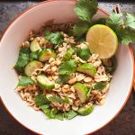 overhead view of a white bowl with ramen noodles, tuna, peanuts and sliced cucumber garnished with cilantro and lime