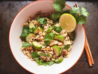 overhead view of a white bowl with ramen noodles, tuna, peanuts and sliced cucumber garnished with cilantro and lime